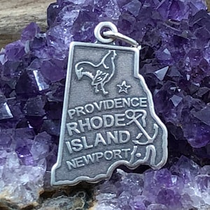 May include: Silver charm shaped like the state of Rhode Island with the words "Providence Rhode Island Newport" and a rooster and anchor design.