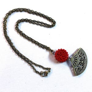 May include: A gold chain necklace with a red and gold pendant. The pendant is a fan shape with a Chinese character on the top and a floral design on the bottom.