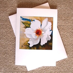May include: A white flower with a red center and green leaves is painted on a card. The background is a light brown color with a blue stripe.