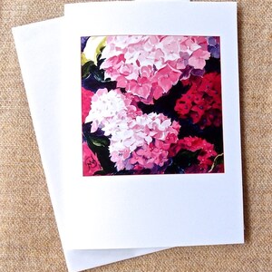 May include: A greeting card featuring a painting of pink and white hydrangeas with a dark background.