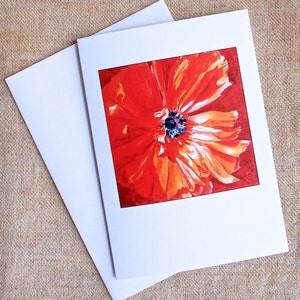 May include: A blank greeting card with a red poppy flower illustration. The poppy has a bright orange center and is surrounded by a white border.