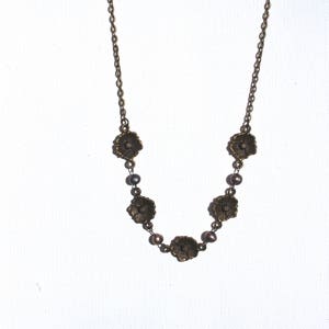 May include: A gold necklace with a chain and five flower-shaped pendants. Each pendant has a dark brown center and is separated by a small, dark brown bead.