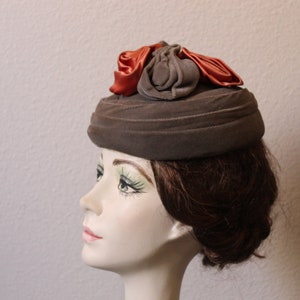 May include: A brown velvet hat with a large orange bow on top. The hat is on a mannequin head with brown hair.