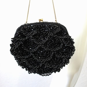 May include: A black beaded evening bag with a chain strap. The bag is round and has a textured surface.