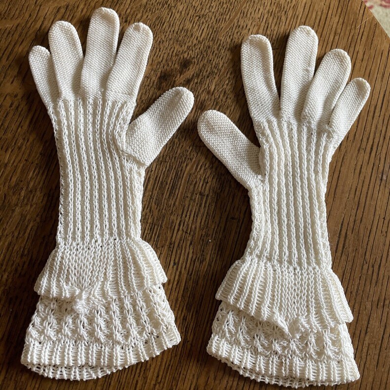 May include: A pair of white crocheted gloves with a ruffled design at the wrist.
