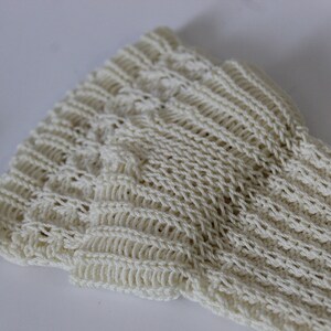 May include: Close-up of a cream-colored knitted fabric with a textured pattern. The fabric is soft and has a delicate, open weave.