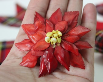 Könnte beinhalten: Eine rote Weihnachtsstern-Blume mit gelben Zentren. Die Blume ist aus Stoff und ist eine Vintage-Weihnachtsdekoration.