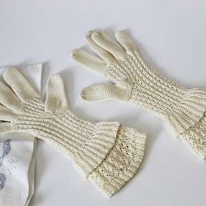 May include: A pair of off-white, long, knitted gloves with a lacy pattern. The gloves have a ruffled cuff.