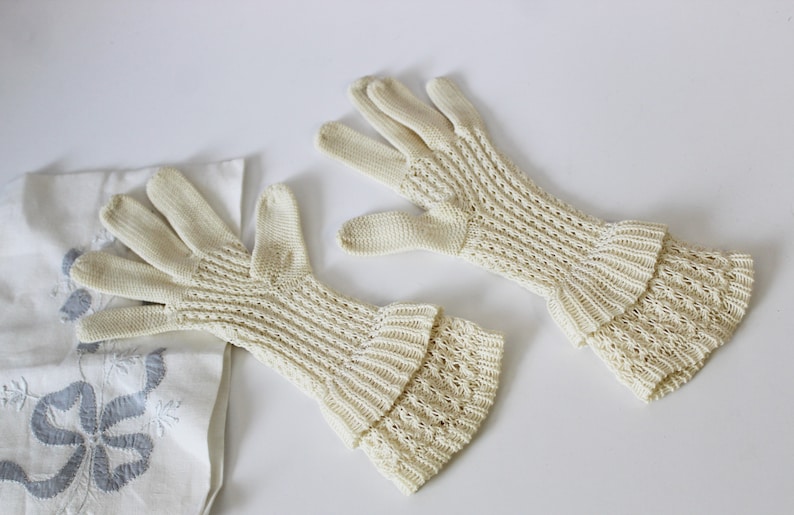May include: A pair of off-white, long, knitted gloves with a lacy pattern. The gloves have a ruffled cuff.