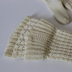 May include: Close-up of a pair of cream-colored knitted gloves. The gloves are made of a delicate, open-weave fabric.