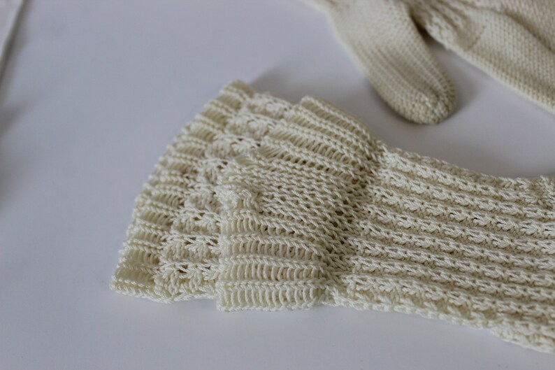 May include: Close-up of a pair of cream-colored knitted gloves. The gloves are made of a delicate, open-weave fabric.