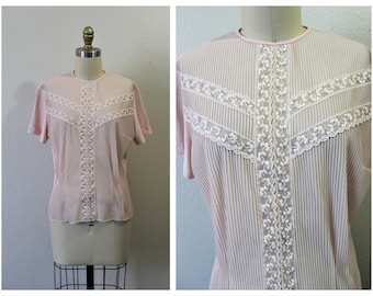 May include: A pink sheer blouse with a white lace overlay. The lace is in a geometric pattern and has a scalloped edge.