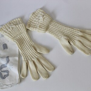 May include: A pair of off-white knitted gloves with a delicate lace pattern. The gloves are long and extend past the wrist.