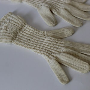 May include: A pair of off-white knitted gloves with a delicate pattern. The gloves are made of a soft, lightweight material and have a comfortable fit.