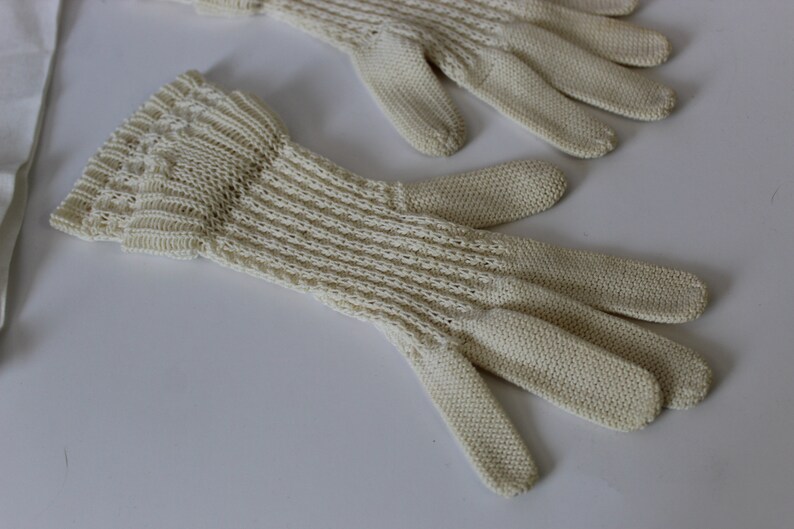 May include: A pair of off-white knitted gloves with a delicate pattern. The gloves are made of a soft, lightweight material and have a comfortable fit.