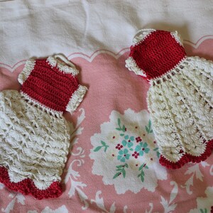 Peut inclure: Deux torchons en crochet en forme de robes. L'un est blanc avec une bordure rouge et l'autre est rouge avec une bordure blanche.
