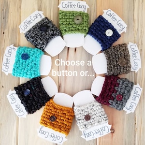 May include: Ten crocheted coffee cup cozies in various colors, including teal, green, brown, black, white, and mustard yellow. Each cozy has a button on the front. The cozies are arranged in a circle on a wooden surface. Choose a button or...