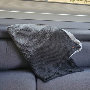 May include: A gray, black, and white striped knitted throw blanket draped over a gray couch.
