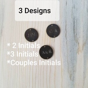 May include: Three metal discs with different initials engraved on them. The discs are on a wooden surface. The text "3 Designs" is at the top of the image. The text "* 2 Initials * 3 Initials * Couples Initials" is below the discs.