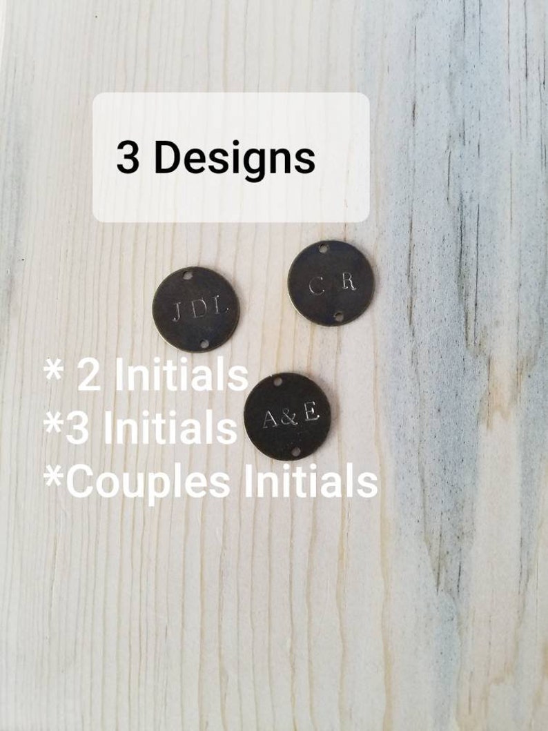 May include: Three metal discs with different initials engraved on them. The discs are on a wooden surface. The text "3 Designs" is at the top of the image. The text "* 2 Initials * 3 Initials * Couples Initials" is below the discs.