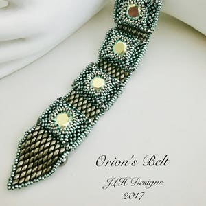 Può includere: Un braccialetto di perline con un design geometrico con perline verdi e dorate. Il braccialetto si chiama "Orion's Belt" ed è di JZH Designs, 2017.