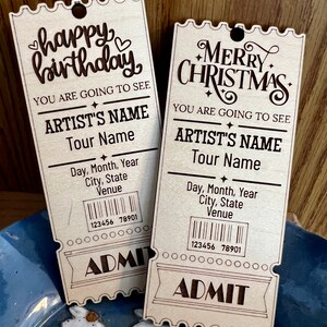 May include: Two wooden ticket stubs with a vintage design. The top stub says "happy birthday" and the bottom stub says "Merry Christmas". Both stubs have the text "You are going to see Artist's Name Tour Name" and a barcode.