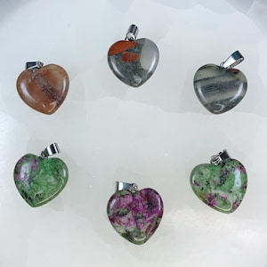 May include: Six heart-shaped gemstone pendants with silver-colored bails. The pendants feature various colors and patterns, including shades of red, green, gray, and brown. The gemstones are polished and smooth, with a glossy finish.