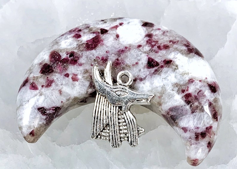 May include: A crescent moon shaped piece of white and pink crystal with a silver Anubis pendant charm.