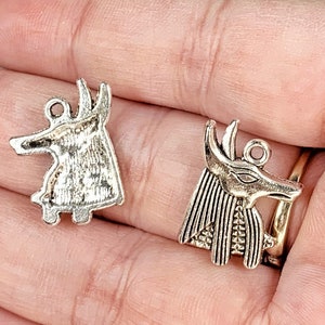 May include: Two silver charm pendants featuring an Egyptian Anubis jackal head design. One pendant is a simple profile, while the other is a more detailed depiction with a headdress.