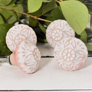 May include: Six pink ceramic drawer knobs with white floral designs. The knobs have a slightly raised edge and a silver screw.