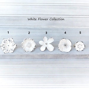 May include: White Flower Collection of five different white metal flower drawer pulls with black accents. The pulls are numbered 1 through 5.
