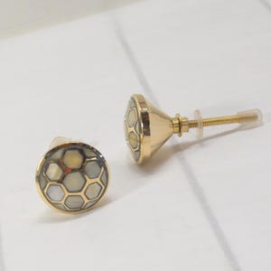 May include: Two decorative cabinet knobs with a gold finish and a honeycomb pattern. The knobs have a round face with a mother-of-pearl inlay and a gold-colored metal base. The screw is approximately 1.5 inches long.