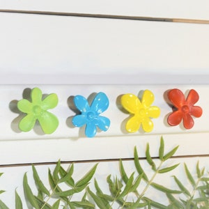 May include: Four colorful flower-shaped knobs in green, blue, yellow, and red. The knobs are attached to a white surface.