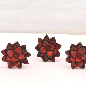 May include: Three decorative, flower-shaped objects with a red and brown color scheme. The objects are arranged in a row against a white background. The flower petals are detailed and textured.