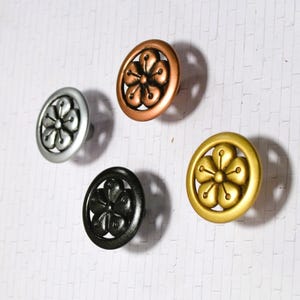 May include: Five decorative cabinet knobs in silver, copper, black, and gold. Each knob features a floral design within a circular frame. The knobs are made of metal and are likely used for furniture or home decor.