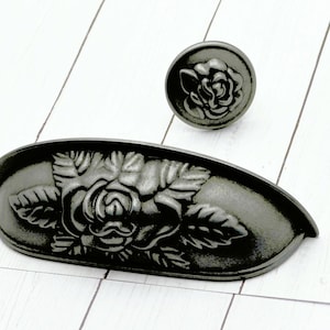 May include: A set of two antique-style cabinet hardware pieces. The set includes a drawer pull and a matching knob, both in a dark gray finish. Each piece features a detailed rose design, adding a touch of vintage charm to any furniture.