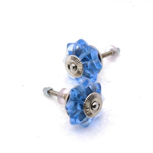 May include: Two blue glass cabinet knobs with a starburst design. Each knob has a silver-colored metal base and a threaded screw for installation. The knobs are set against a white background.
