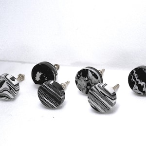 May include: Six round cabinet knobs with a black and white marbled design. The knobs have a silver-colored stem and are set against a white background. The knobs are a decorative hardware element.