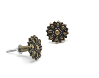 May include: Two antique brass-colored flower-shaped cabinet knobs on a white background. One knob is lying on its side, showing the screw, and the other is upright. The knobs have a detailed floral design.