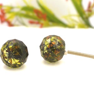 May include: Two faceted, decorative cabinet knobs with a mosaic-like design in shades of green, gold, and orange. Each knob has a metal screw for installation. The knobs are set against a white background.