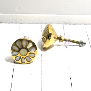 May include: Two gold-toned cabinet knobs with a floral design. Each knob features a central cream-colored circle surrounded by petal-shaped mother-of-pearl inlays. One knob is fully assembled with a screw and nut, while the other is shown from the front.