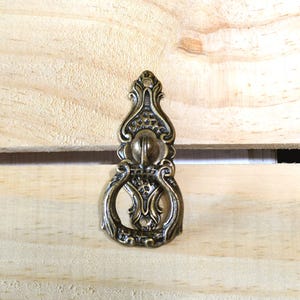 May include: Ornate antique brass drawer pull with a decorative design. The pull features a central ball and intricate scrollwork, ideal for adding a vintage touch to furniture. The hardware is approximately 4 inches in length.