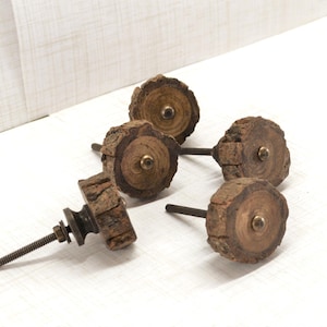 May include: A collection of five rustic wooden cabinet knobs. Each knob features a circular, bark-edged wooden face with a brass-colored center. The knobs are attached to threaded rods with nuts and washers, suggesting they are ready for installation.