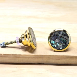 May include: A white ceramic mug with a black handle and the text "But First, Coffee" in a bold, black font. The mug is set against a blurred background, suggesting a cozy setting.