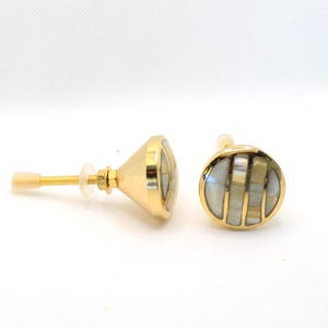 May include: Two gold-toned cabinet knobs with a mother-of-pearl inlay. One knob is cone-shaped, the other is round. The knobs have a gold screw and a clear plastic washer. The knobs are for furniture and home decor.