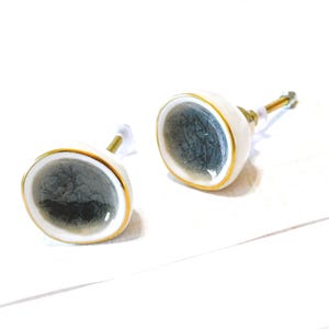 May include: Two ceramic cabinet knobs. Each knob has a white base with a gold trim and a dark gray, crackled center. The knobs have brass hardware for installation. These decorative knobs are ideal for adding a unique touch to furniture.