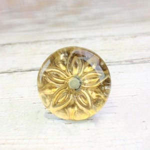 May include: A round, clear glass knob with a gold flower design. The knob is perfect for adding a touch of elegance to any cabinet or drawer.