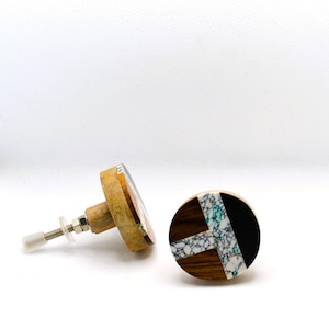 May include: Two decorative wooden cabinet knobs. One knob features a circular design with a black section, a white and teal section, and a brown wood section. The other knob has a similar design with a light-colored wood base.