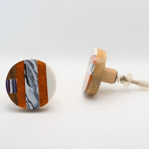 May include: Two decorative cabinet knobs. One knob is round with a white, orange, gray, and brown design. The other knob is shown from the side, revealing a wooden base and screw. Hardware for furniture.