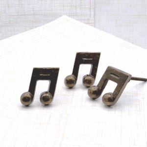 May include: Three bronze-colored musical note cabinet knobs. Each knob features a detailed musical note design with a rounded base. The knobs are set against a white background, ideal for a music-themed decor.